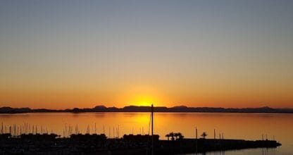 Espectacular atardecer dorado sobre la laguna del Mar Menor con siluetas de veleros en el puerto, vista desde La Manga Realty