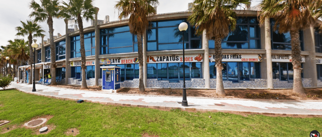 Edificio comercial acristalado con palmeras y locales de moda en D'Costa Puerto y Playa, La Manga del Mar Menor