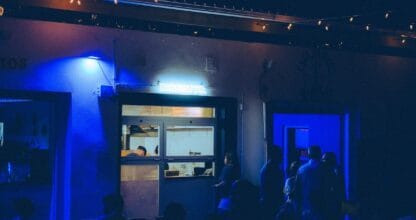Ambiente nocturno de Disfruto pizzeria con luz azul neón, letrero luminoso, público y cocina a la vista en La Manga