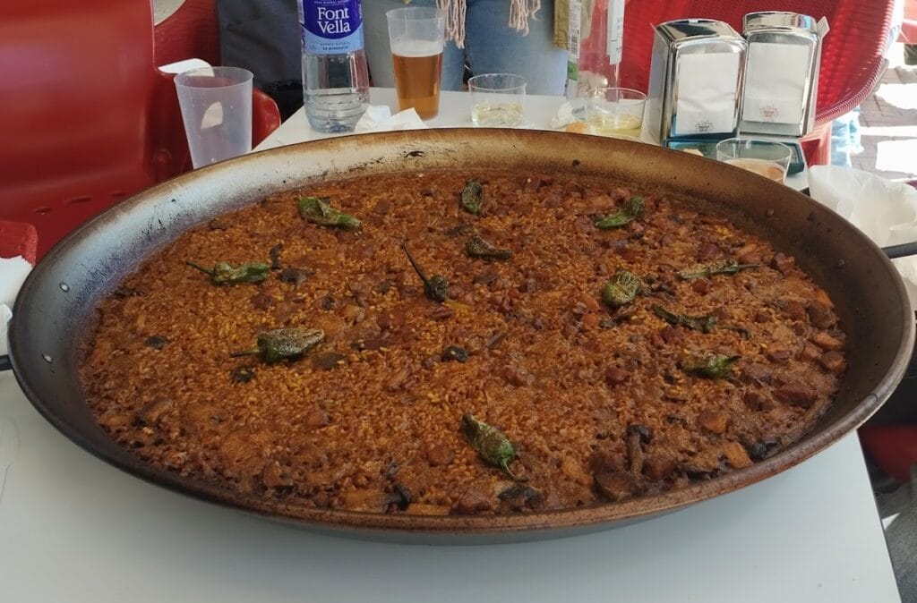Gran paella de arroz con carne en bandeja de hierro con pimientos verdes fritos en El arroz todo locura, La Manga