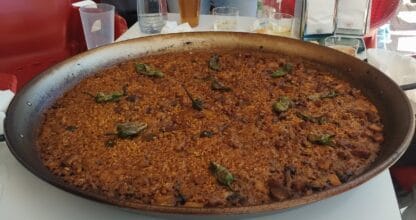 Gran paella de arroz con carne en bandeja de hierro con pimientos verdes fritos en El arroz todo locura, La Manga