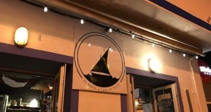Fachada nocturna de El Barco en Cabo de Palos con logo de velero iluminado y puertas abiertas mostrando el interior del local