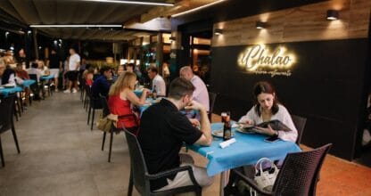 Terraza nocturna del restaurante El Chalao llena de comensales en mesas con mantel azul y rótulo luminoso en pared oscura