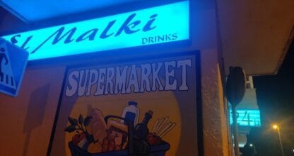 Fachada iluminada de noche del supermercado El Malki Drinks en La Manga del Mar Menor