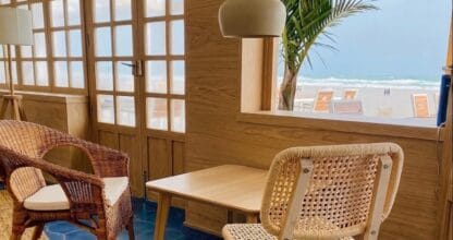 Rincón interior de El Nido La Manga con sillas de ratán y vistas directas al mar a través de ventana de madera
