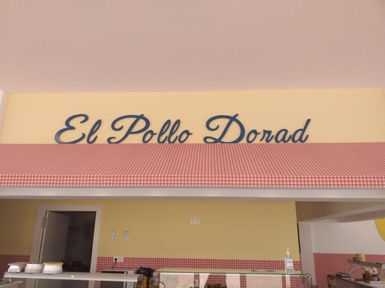 Interior de El Pollo Dorado La Manga con mostrador de servicio y rótulo retro amarillo con cuadros rojos y blancos