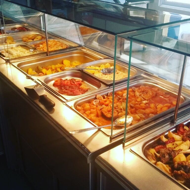 Mostrador de buffet de El Pollo Dorado La Manga con bandejas de guisos, mariscos, patatas y platos caseros calientes