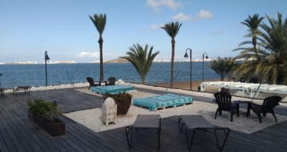 Terraza de madera de El Secreto del Agua con tumbonas y camas balinesas junto al Mar Menor, palmeras y vistas panorámicas al atardecer