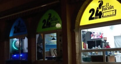Fachada nocturna de El Tucan 24 Hours en La Manga del Mar Menor con rótulos luminosos de colores y diana de dardos al fondo