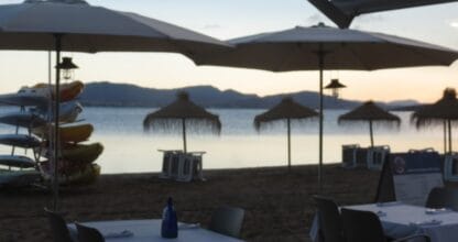 Terraza de la Escuela de Vela con Cafetería junto a la playa del Mar Menor al atardecer, con kayaks y sombrillas de paja
