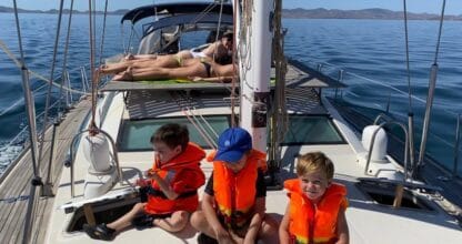 Tres niños con chalecos salvavidas naranjas en cubierta de velero con la Escuela Náutica El Marino, La Manga del Mar Menor