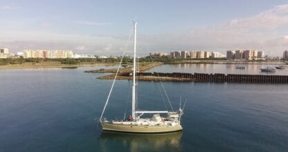 Velero de la Escuela Náutica Wayucharter navegando en aguas tranquilas con el skyline de La Manga del Mar Menor al fondo