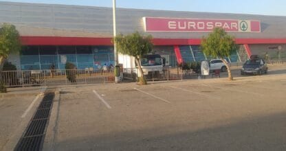 Fachada del centro comercial con Expert Alttamar y supermercado en La Manga del Mar Menor al atardecer con aparcamiento
