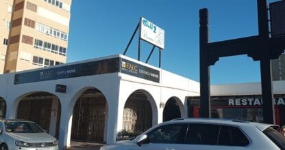 Fachada exterior de la oficina de FALC Real Estate con rótulos en español y alemán, edificio blanco con arcos en La Manga del Mar Menor