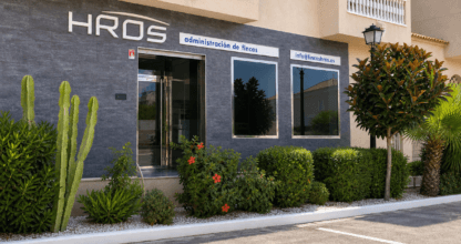 Oficina moderna de Fincas HRos con fachada de piedra oscura, logotipo en relieve y jardín con cactus en La Manga del Mar Menor