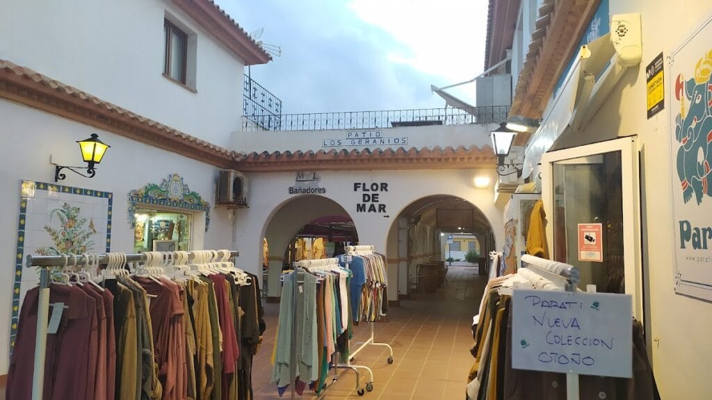 Patio Los Geranios en La Manga del Mar Menor con tienda Flor de Mar de bañadores y percheros de ropa bajo arcos blancos