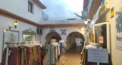 Patio Los Geranios en La Manga del Mar Menor con tienda Flor de Mar de bañadores y percheros de ropa bajo arcos blancos
