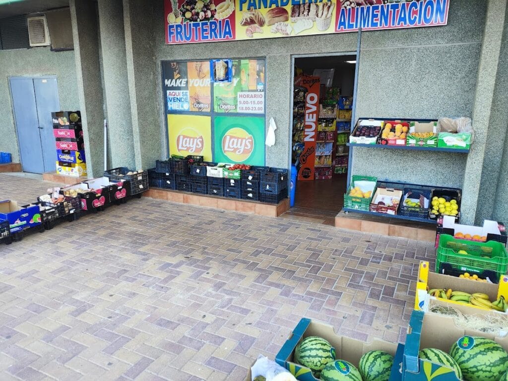 Exterior de la Frutería Costa Azul en La Manga con cajas de frutas, sandías y carteles de panadería y alimentación