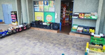 Exterior de la Frutería Costa Azul en La Manga con cajas de frutas, sandías y carteles de panadería y alimentación