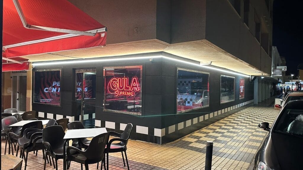 Fachada nocturna de Gula Supreme La Manga con rótulo neón rojo, terraza exterior y toldo rojo en esquina de calle