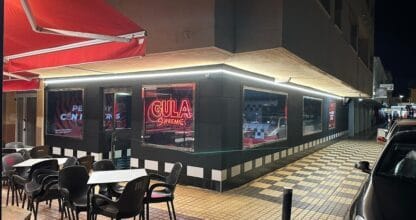 Fachada nocturna de Gula Supreme La Manga con rótulo neón rojo, terraza exterior y toldo rojo en esquina de calle