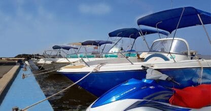Flota de lanchas motoras y moto de agua de Happy Boat amarradas en el pantalán de La Manga del Mar Menor bajo cielo azul