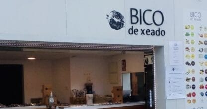 Fachada exterior de la heladería Bico de Xeado con mostrador de madera acanalada, carta de sabores y logo en edificio blanco