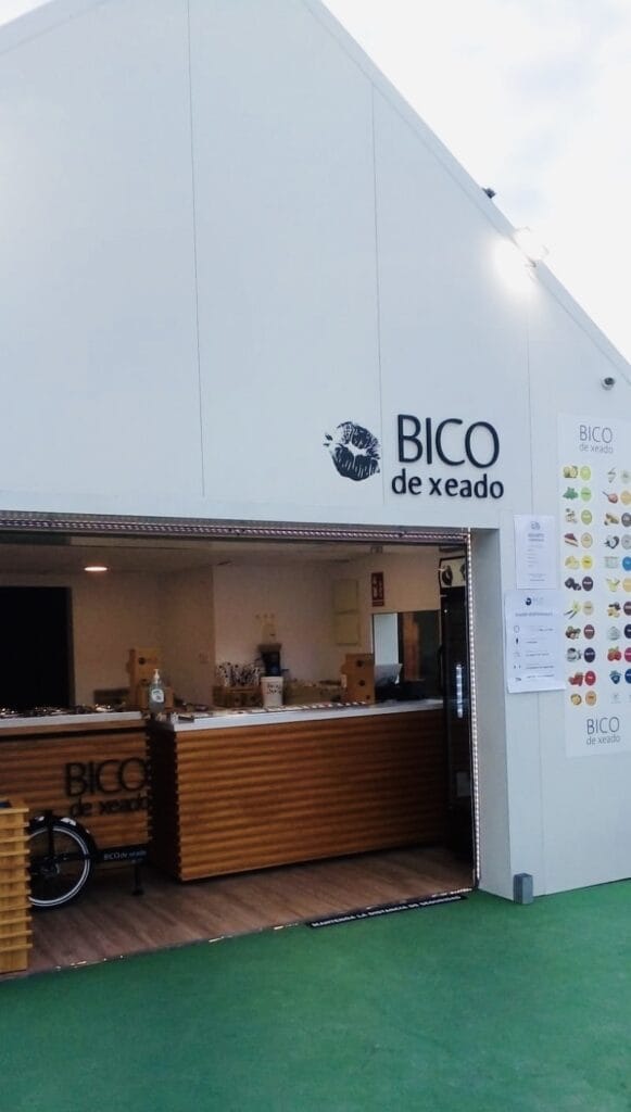 Fachada exterior de la heladería Bico de Xeado con mostrador de madera acanalada, carta de sabores y logo en edificio blanco