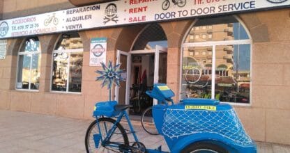 Fachada de HobbyBike La Manga con triciclo azul de alquiler en la puerta, tienda de bicicletas con reparación y venta