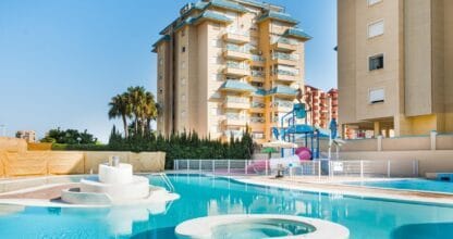 Piscina con toboganes y zona acuática infantil del Hotel Bakour La Manga Splash con torre de apartamentos al fondo en La Manga