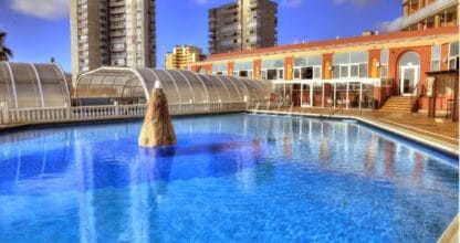 Piscina exterior con fuente del Hotel y Spa Entremares en La Manga del Mar Menor con cubierta acristalada y edificios al fondo