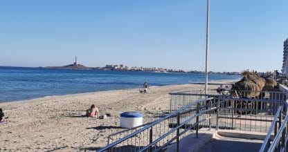 Vista de la playa de La Manga del Mar Menor desde Jijonenca Helado Artesano con bañistas en la arena y el faro de Cabo de Palos al fondo