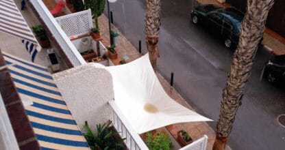 Terraza de alojamiento José Roca Legaz en La Manga del Mar Menor vista desde arriba, con toldos blancos, palmeras y calle residencial bajo la lluvia