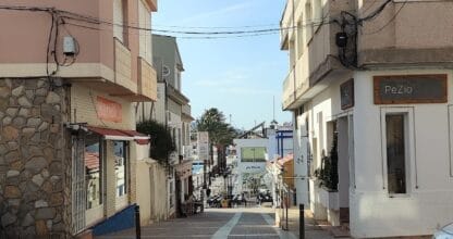Calle típica de Cabo de Palos con locales comerciales a ambos lados y vistas al mar mediterráneo al fondo en día soleado