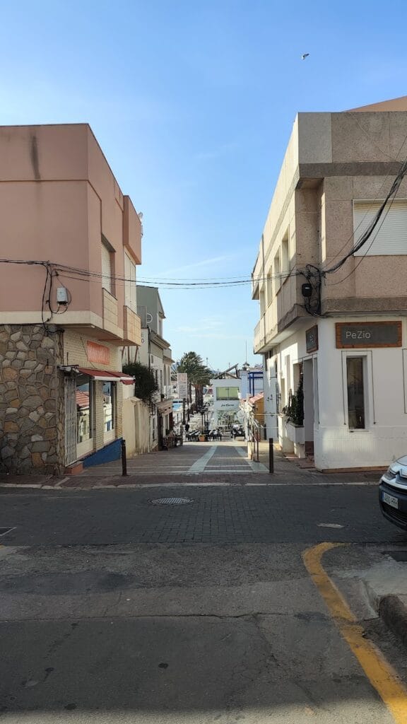 Calle típica de Cabo de Palos con locales comerciales a ambos lados y vistas al mar mediterráneo al fondo en día soleado