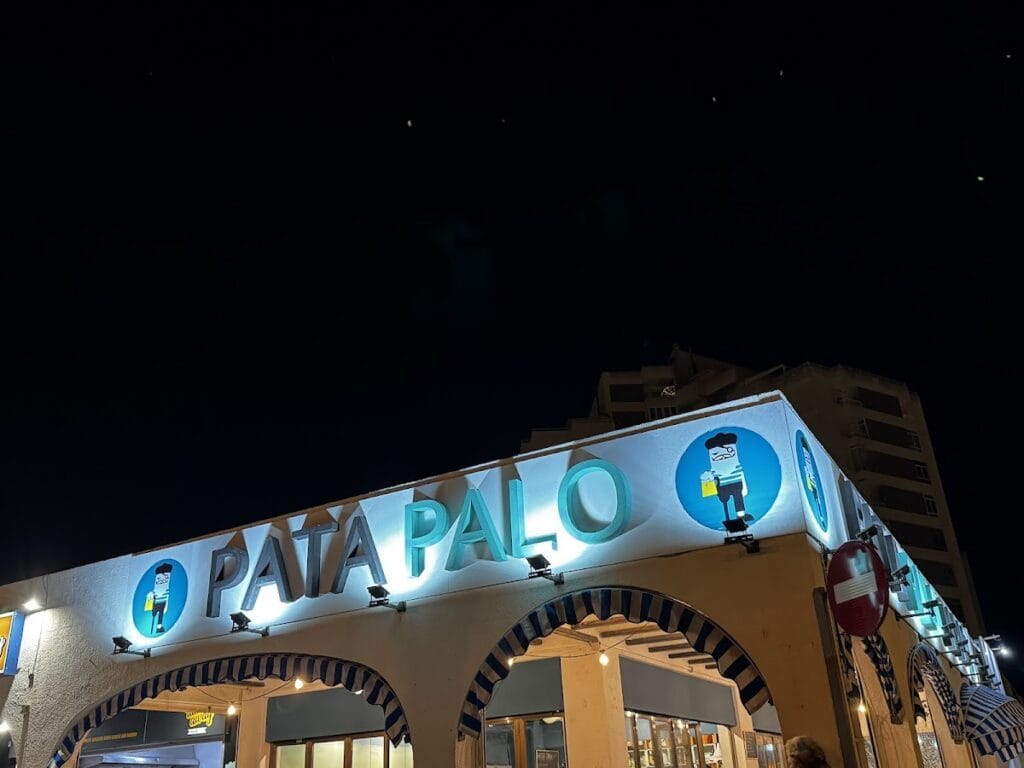 Fachada nocturna iluminada de restaurante Ke rico nico con letrero azul luminoso y arcos decorativos en La Manga del Mar Menor
