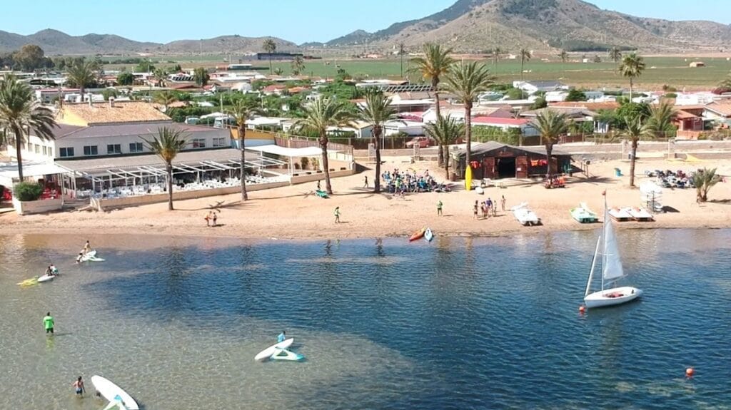 Vista aérea de playa del Mar Menor con velero, tablas de paddle surf y alumnos de KSURF La Manga en la orilla