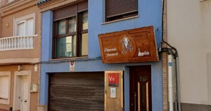 Fachada de La Casita Azul pintada en azul con cartel de madera de apartamentos vacacionales en calle de La Manga del Mar Menor