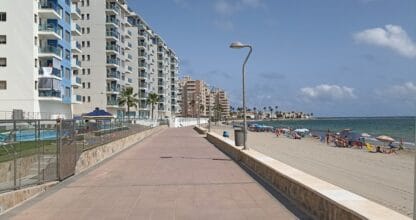 Paseo marítimo con edificios de apartamentos junto a la playa y bañistas en La Manga del Mar Menor