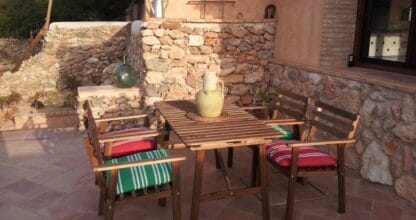 Terraza rústica con mesa y sillas de madera junto a pared de piedra en alojamiento La Jordana, La Manga del Mar Menor