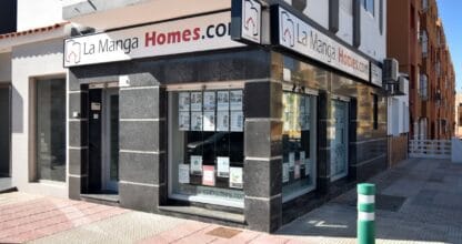 Fachada en esquina de La Manga Homes con escaparates de propiedades en venta y alquiler, inmobiliaria en La Manga del Mar Menor