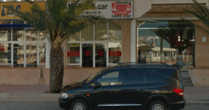 Local de La Manga Rent a Car con vehículos aparcados en la puerta y palmera en la acera de La Manga del Mar Menor