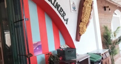 Fachada colorida de La Marinera con arco a rayas rojas y turquesas, letrero y figura decorativa de bocadillo en la pared