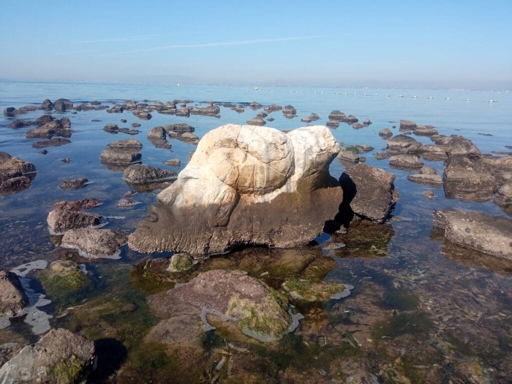 La Piedra del Fauno, gran roca singular emergiendo entre piedras en la orilla del Mar Menor con horizonte azul