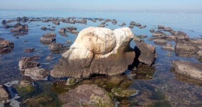 La Piedra del Fauno, gran roca singular emergiendo entre piedras en la orilla del Mar Menor con horizonte azul
