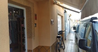 Fachada de La Tienda de Rafa en La Manga del Mar Menor, pequeño local de ropa con puerta abierta, toldo y bicicleta aparcada en la acera