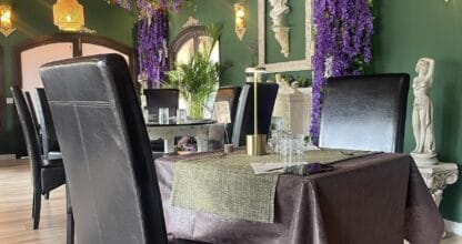 Comedor de La Zorra Gourmet decorado con flores de glicinia morada colgantes, paredes verdes y esculturas clásicas