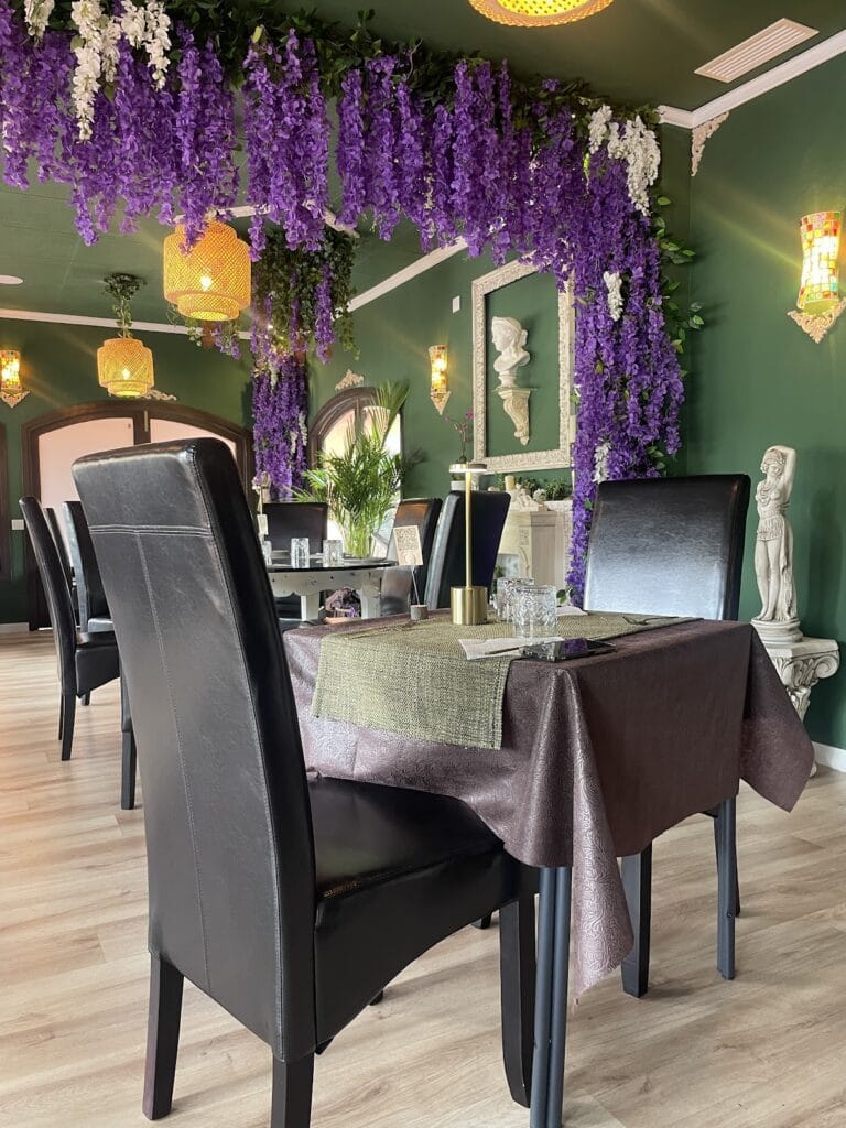 Comedor de La Zorra Gourmet decorado con flores de glicinia morada colgantes, paredes verdes y esculturas clásicas