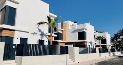 Viviendas unifamiliares de diseño moderno con fachada blanca y revestimiento de madera y palmeras en urbanización de La Manga del Mar Menor