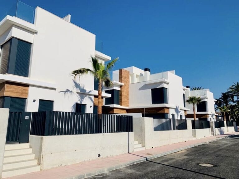 Viviendas unifamiliares de diseño moderno con fachada blanca y revestimiento de madera y palmeras en urbanización de La Manga del Mar Menor